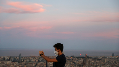 Un jóven, con mascarilla, toma una foto con su 'smartphone', con la ciudad de Barcelona al fondo. REUTERS/Nacho Doce Un jóven, con mascarilla, toma una foto con su 'smartphone', con la ciudad de Barcelona al fondo. REUTERS/Nacho Doce