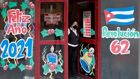 Una mujer se asoma desde la entrada a una cafetería estatal decorada con carteles alegóricos al fin de año y al aniversario 62 del triunfo de la Revolución cubana, en La Habana (Cuba). EFE/ Yander Zamora Una mujer se asoma desde la entrada a una cafetería estatal decorada con carteles alegóricos al fin de año y al aniversario 62 del triunfo de la Revolución cubana, en La Habana (Cuba). EFE/ Yander Zamora