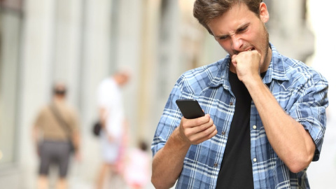 Un hombre, que se encuentra mirando un teléfono móvil, muestra una mueca molesta. Shutterstock / Antonio Guillem