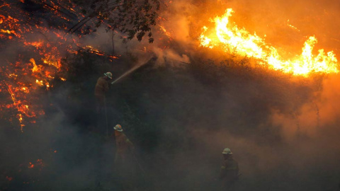 Varios bomberos utilizan las mangueras para contener el fuego en los alrededores del pueblo de Fato. | RAFAEL MARCHANTE (EFE)
