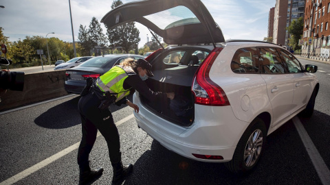 Una agente de la Policía Nacional registra el maletero de un coche durante uno de los controles en las salidas de Madrid. - EFE