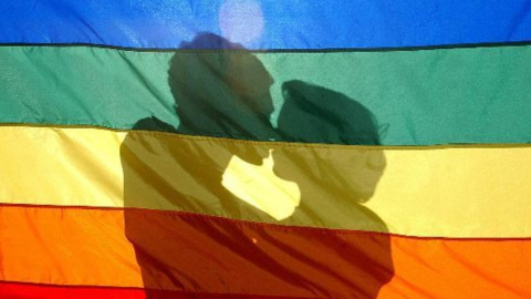 Una pareja se besa tras la bandera del arcoíris, símbolo del movimiento LGTBI. Una pareja se besa tras la bandera del arcoíris, símbolo del movimiento LGTBI.