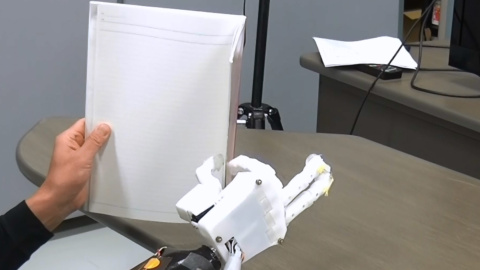 El sujeto amputado sostiene un cuaderno usando la prótesis de mano mioeléctrica con control de sinergia muscular El sujeto amputado sostiene un cuaderno usando la prótesis de mano mioeléctrica con control de sinergia muscular
