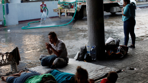 Un trabajador municipal riega la calle mientras los migrantes de América Central duermen en el suelo del parque central Miguel Hidalgo, México. / Reuters