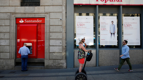 Un hombre utiliza un cajero automático del Banco Santander junto a una oficina del Popular, en Madrid. /Juan Medina Un hombre utiliza un cajero automático del Banco Santander junto a una oficina del Popular, en Madrid. /Juan Medina