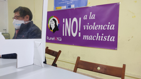 Vladimir Paspuel, presidente de la Asociación Rumiñahui, observa el teléfono móvil en una mesa donde recibe a los jóvenes de las bandas. Al fondo un cartel contra la violencia machista. - Guillermo Martínez
