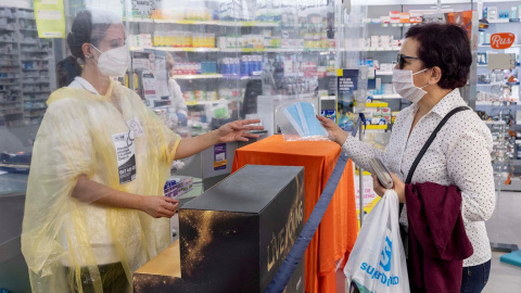 Una empleada de farmacia entrega de forma gratuita dos mascarillas a una pensionista mediante la receta electrónica. /EFE Una empleada de farmacia entrega de forma gratuita dos mascarillas a una pensionista mediante la receta electrónica. /EFE