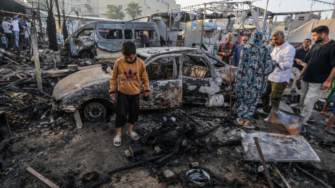 Palestinos inspeccionan coches quemados tras un ataque del ejército israelí contra tiendas para desplazados internos, a 14 de octubre de 2024.