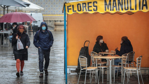 Dos personas en la terraza de un bar protegidas de la lluvia por un toldo de un puesto de flores. Dos personas en la terraza de un bar protegidas de la lluvia por un toldo de un puesto de flores.