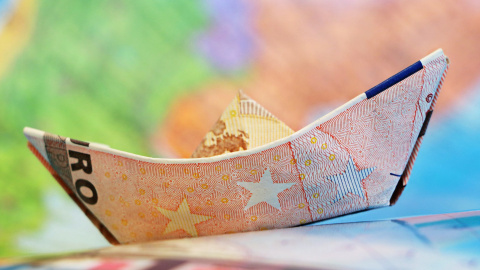 Imagen recurso de un barco de papel hecho con un billete. Al fondo, un mapamundi difuminado. - Pixabay Imagen recurso de un barco de papel hecho con un billete. Al fondo, un mapamundi difuminado. - Pixabay