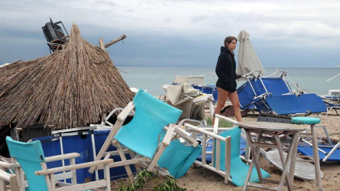 Una mujer camina entre sillas volcadas por el temporal en Grecia. EFE/EPA/VERVERIDIS VASSILIS