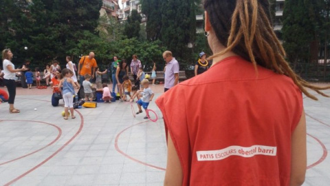 Una monitora observa diversos niños y familiares en el patio de una escuela.