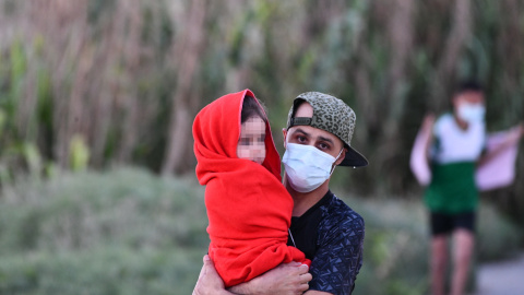 Un hombre migrantes coge en brazos a una menor, a 17 de mayo de 2021