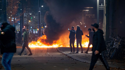 La gente se para cerca de objetos en llamas después de que una protesta en Róterdam contra la 'política 2G' se convirtiera en disturbios La gente se para cerca de objetos en llamas después de que una protesta en Róterdam contra la 'política 2G' se convirtiera en disturbios