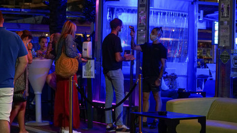 Un empleado toma la temperatura a un joven que hace cola para entrar en un pub en el puerto deportivo de Marbella. Fotografía de archivo. Un empleado toma la temperatura a un joven que hace cola para entrar en un pub en el puerto deportivo de Marbella. Fotografía de archivo.