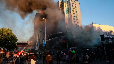 Los manifestantes frente a un edificio en llamas mientras los bomberos trabajan para apagar el fuego durante una protesta contra el gobierno en Santiag. REUTERS / Henry Romero