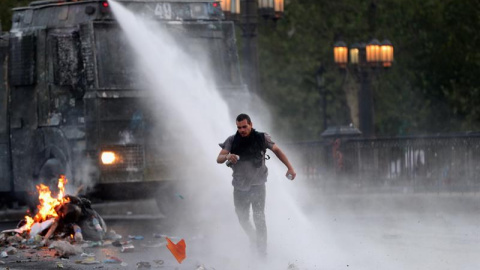 Un manifestante huye del chorro de agua lanzado por la policía durante una nueva jornada de protestas contra el Gobierno del presidente chileno Eduardo Piñera este sábado, en Santiago (Chile). El alza en el precio del pasaje del metro de Santiago prend Un manifestante huye del chorro de agua lanzado por la policía durante una nueva jornada de protestas contra el Gobierno del presidente chileno Eduardo Piñera este sábado, en Santiago (Chile). El alza en el precio del pasaje del metro de Santiago prend