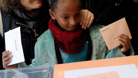 Una niña deposita el voto de una mujer en la urna. / Reuters.