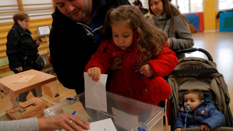 Una niña deposita el voto de su padre, que la sostiene en brazos. / Reuters