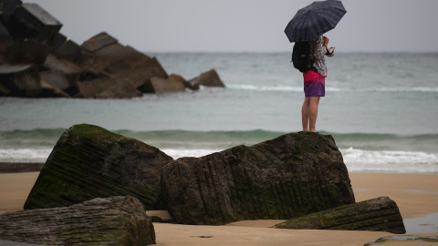 Un joven se protege con un paraguas en la playa de la Zurriola de San Sebastián. Un joven se protege con un paraguas en la playa de la Zurriola de San Sebastián.