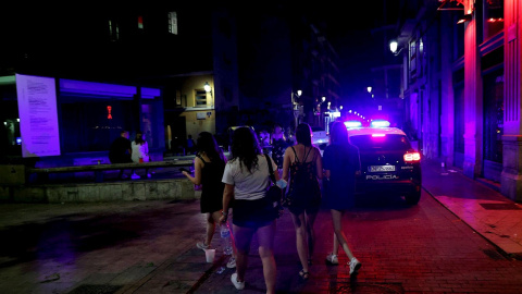Varios jóvenes turistas pasan ante un coche de policía esta madrugada en la calle Caballeros del barrio de El Carmen de València.