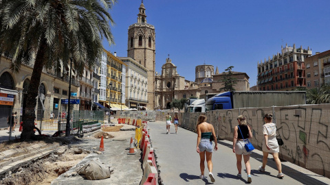 Varias turistas pasean por el asfaltado levantado y las vallas que rodean completamente la céntrica plaza de la Reina de València por las obras que se llevan a cabo para remodelarla. Varias turistas pasean por el asfaltado levantado y las vallas que rodean completamente la céntrica plaza de la Reina de València por las obras que se llevan a cabo para remodelarla.