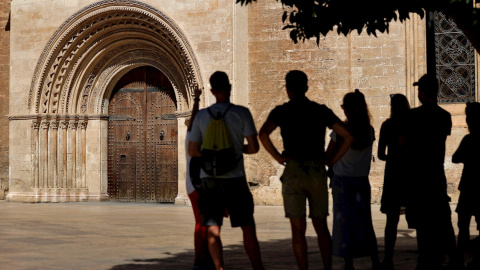 22/07/2021.- Un grupo de turistas atienden las explicaciones de su guía ante la puerta románica de la Catedral de Valencia.