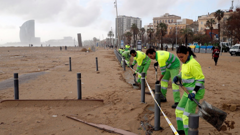 Trabajadores de la limpieza realizan su trabajo este jueves en la playa de la Barceloneta, gravemente afectada por la borrasca Gloria, que se ha cebado especialmente con el frente marítimo de Barcelona. EFE/ Toni Albir