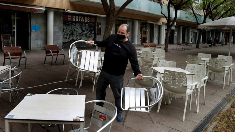 Un camarero prepara la terraza del restaurante donde trabaja en L'Hospitalet de Llobregat para atender a sus clientes en el turno de 13:00h a 16:30h, uno de los dos horarios permitidos para la restauración.