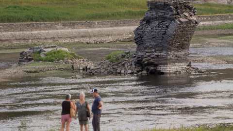 Tres personas junto al río Miño, cuyo bajo caudal ha dejado a la vista las ruinas del antiguo Portomarín, que en los años 60 del siglo pasado fue anegado por el embalse de Belesar Tres personas junto al río Miño, cuyo bajo caudal ha dejado a la vista las ruinas del antiguo Portomarín, que en los años 60 del siglo pasado fue anegado por el embalse de Belesar