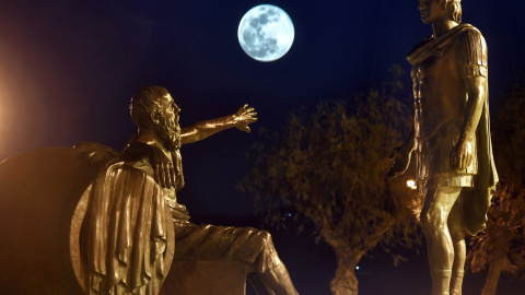 Vista de la luna de nieve, detrás de estatuas del antiguo filósofo cínico griego Diogenes, y el antiguo rey macedonio griego Alejandro Magno en la ciudad de Corinto, Peloponeso | EFE/Vassilis Psomas