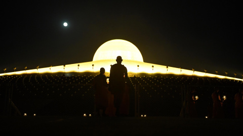 Monjes budistas que llevan velas encendidas mientras la luna llena se levanta durante las oraciones para conmemorar el Día de Makha Bucha en el templo de Wat Phra Dhammakaya, cerca de Bangkok | AFP/ Lillian Suwanrumpha