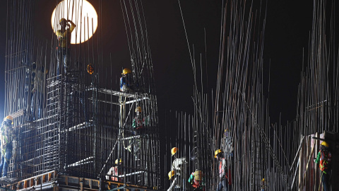 La luna de nieve se eleva cuando unos obreros de la construcción trabajan en una obra en Kolkata, Calcuta, India | AFP/ Dibyangshu Sarkar