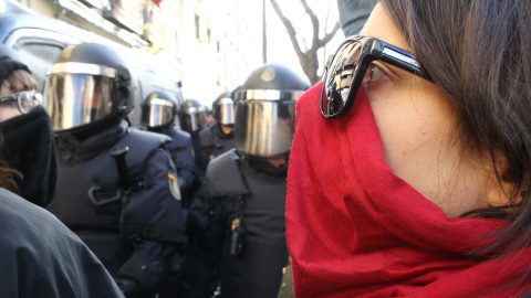 Una mujer mira hacia los agentes antidisturibios de la Policía Nacional presenciados en la inmediaciones de la calle Argumosa de Madrid, donde se manifestan activistas de la plataforma 'Stop Desahucios' ante la previsión de varios desahucios decretados 