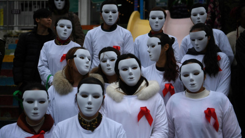 Voluntarios con máscaras blancas y cintas rojas en sus camisetas participan en un evento para crear conciencia sobre el Sida en Chongqing.- REUTERS