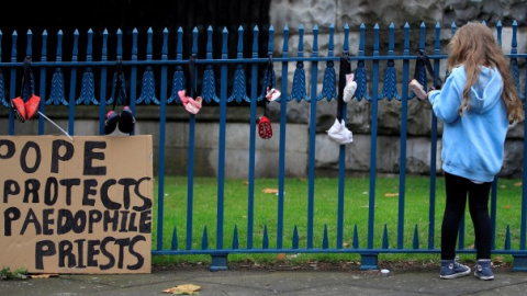 Una niña cuelga un zapato de bebé en una valla para protestar contra los abusos de la Iglesia. - REUTERS Una niña cuelga un zapato de bebé en una valla para protestar contra los abusos de la Iglesia. - REUTERS