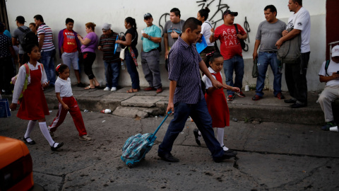 Niñas camino a la escuela pasan por delante de los migrantes que esperan ingresar a la Comisión Mexicana de Asistencia a Refugiados en Tapachula. / Reuters