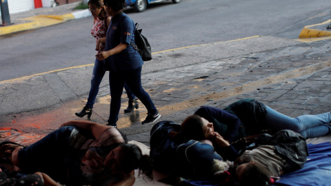 Dos mujeres caminan por la calle mientras las migrantes de América Central duermen en el suelo en el Parque Central Miguel Hidalgo, en México. / Reuters
