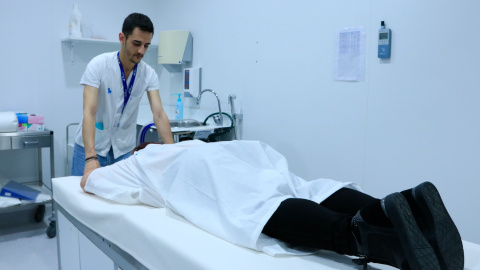 Un col·laborador del projecte QUSTom ajuda una dona a col·locar-se boca avall en el llit per a una nova tècnica basada en ultrasons tomogràfics en 3D i supercomputació per a la detecció precoç del càncer de mama, a l'Hospital Vall d'Hebron. Un col·laborador del projecte QUSTom ajuda una dona a col·locar-se boca avall en el llit per a una nova tècnica basada en ultrasons tomogràfics en 3D i supercomputació per a la detecció precoç del càncer de mama, a l'Hospital Vall d'Hebron.