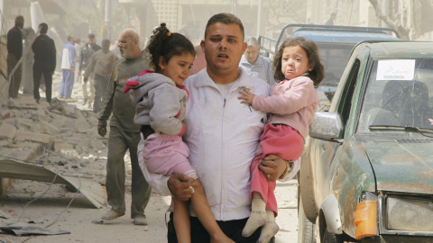 Un hombre coge a dos niñas mientras se apresura a buscar un refugio después de que el barrio de al-Thawra haya sido golpeado./ REUTERS / Ammar Abdullah
