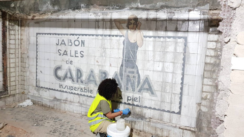 Operaria limpia los azulejos del mural publicitario datado en los años 20 y descubierto en las obras de la estación de metro Sevilla, en Madrid. / Consejería de Cultura Operaria limpia los azulejos del mural publicitario datado en los años 20 y descubierto en las obras de la estación de metro Sevilla, en Madrid. / Consejería de Cultura