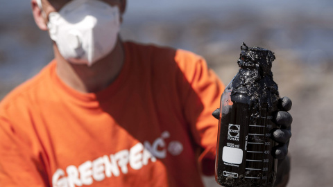 Un miembro de Greenpeace enseña un bote con muestras del combustible que ha llegado en las últimas horas a la playa de Venegueras, en el municipio grancanario de Mogán, que se cree que procede del pesquero ruso hundido Oleg Naydenov. EFE