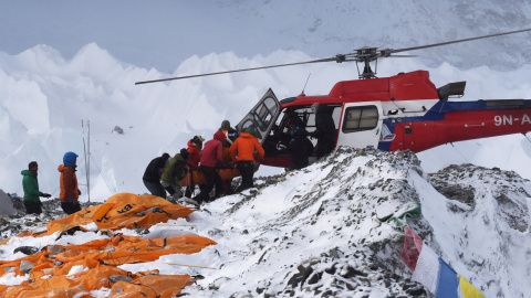Una persona herida es subida a un helicóptero de rescate en el campamento base del Everest mientras los cadáveres de montañeros esperan ser trasladados, envueltos en sacos naranja.- AFP PHOTO / ROBERTO SCHMIDT