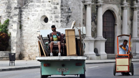 Un hombre juega con su teléfono móvil mientras viaja en la parte trasera de un camión en La Habana. EFE/Alejandro Ernesto