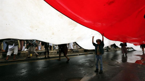 Cientos de personas llevan una bandera nacional durante una manifestación en contra de la violaciones al alto el fuego en Saná, Yeme. EFE/Yahya Arhab