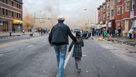 Un hombre camina con su hija en medio de las protestas por la muerte de Freddie Gray. EFE