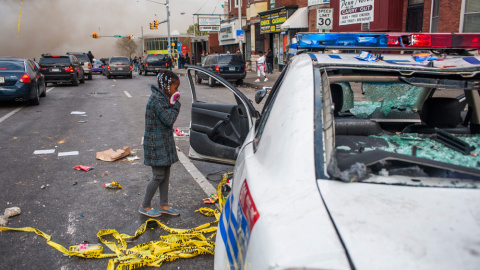 Una niña observa un vehículo de la policía que fue atacado durante protestas tras del funeral de Freddie Gray el lunes en Baltimore. EFE