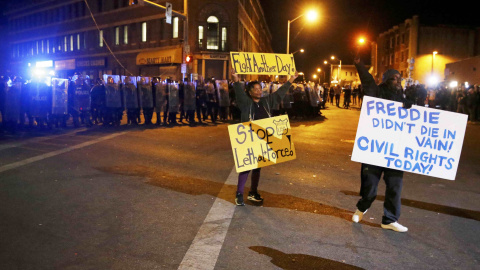 Protesters hold up signs in front of a line of police in Baltimore, Maryland. REUTERS/Jim Bourg
