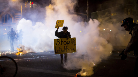 A protester holds a sign as clouds of smoke and crowd control agents rise, shortly after the deadline for a city-wide curfew passed in Baltimore, Maryland. REUTERS/Eric Thayer