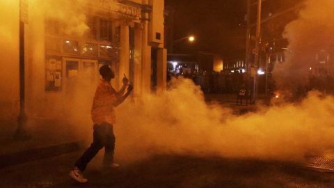A protester responds as clouds of smoke and crowd control agents rise shortly after the deadline for a city-wide curfew passed in Baltimore, Maryland. REUTERS/Jim Bourg